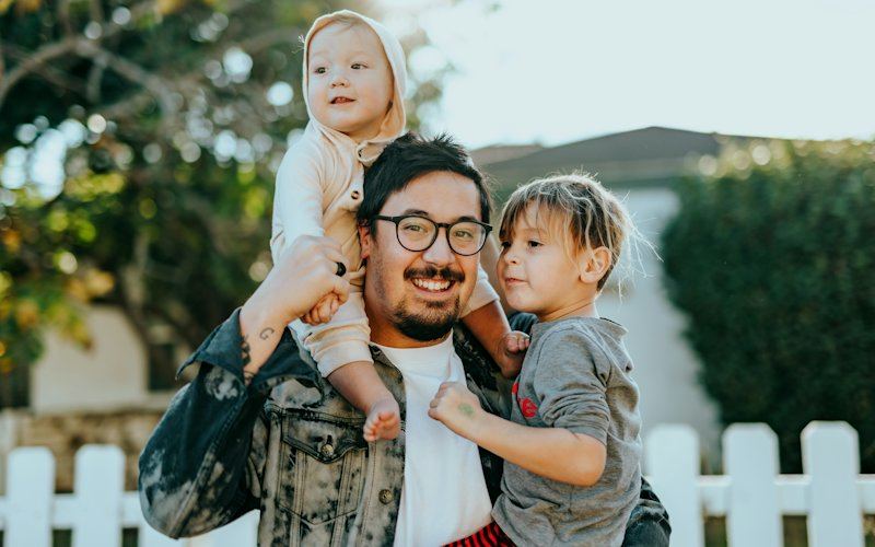Pai com os dois filhos ao colo à porta de casa